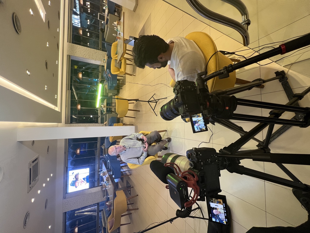 Behind the scenes: filming an on-camera interview with the film's subject at night, camera and audio equipment in the foreground